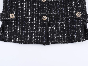 Close-up of black and white tweed fabric with embossed golden lion head metal buttons
