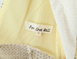 Close-up of yellow polka dot fabric with white floral lace embroidery and brand label