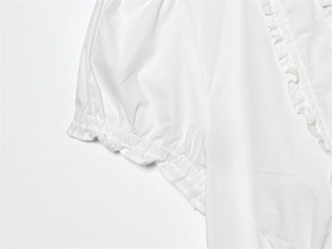 Macro detail of white blouse featuring ruffle trim and elastic bubble sleeve cuffs