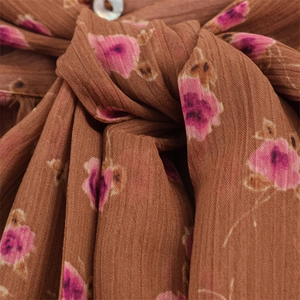 Detail of floral brown top with pleated fabric, shell button, and bow tie neck design