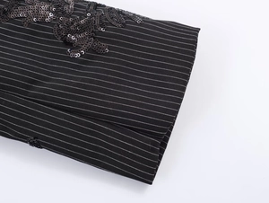 Close-up of black pinstripe fabric with intricate sequin embroidery and vine patterns