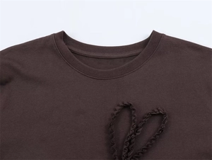 Close-up of crew neckline and wavy 3D textured bow detail on dark brown knit T-shirt