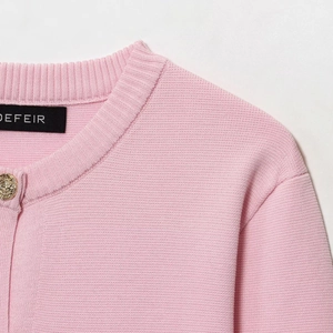 Dettaglio di cardigan in maglia rosa con scollo rotondo e bottone in metallo dorato