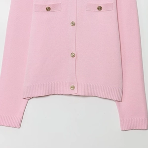 Dettaglio del cardigan rosa in maglia con eleganti bottoni dorati e finte tasche