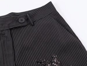 Detail of black pinstripe trousers featuring sequin floral embroidery and button closure