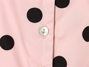Close-up of pearl-like button and black polka dot pattern on pink long sleeve jacket fabric