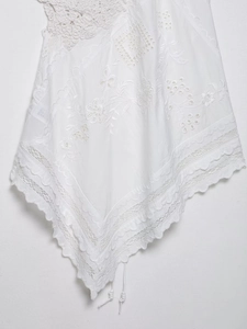 Detail of white bohemian top featuring crochet flowers, floral embroidery and lace hem