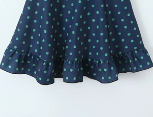 Detail of the navy blue dress ruffle hem featuring green floral patterns on woven fabric