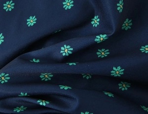 Macro shot of dark blue silky fabric with green floral pattern and soft pleats
