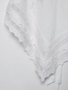 Close-up of white floral lace embroidery and scalloped edges on a minimalist cotton top