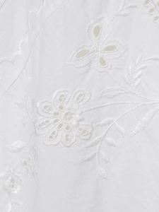 Detail of white embroidered fabric with floral eyelet patterns and intricate lace texture