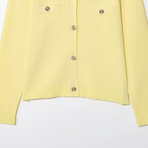 Dettaglio del cardigan in maglia giallo chiaro con bottoni dorati e polsini a coste bianchi