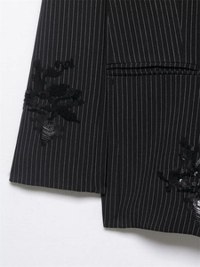 Detail of pinstripe blazer featuring black sequin floral embroidery on woven fabric