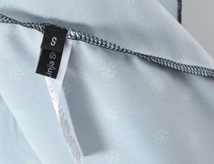 Detailed macro shot of the side seam, wash tags, and size label S on a light blue floral dress
