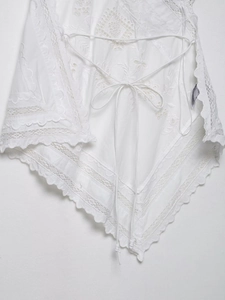Detail of white asymmetric top showing floral lace embroidery and lace-up drawstring detail