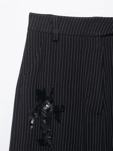 Detail of pinstripe trousers featuring black sequin embroidery and belt loops