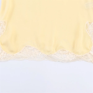 Close-up of pale yellow satin fabric with intricate white floral lace trim on the hemline