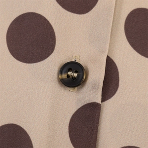 Detailed macro view of beige satin blouse with large dark brown polka dots and button