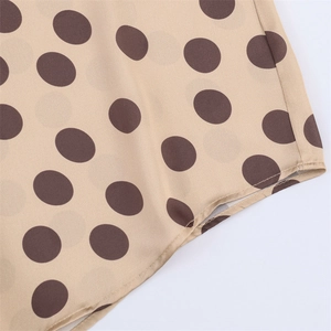 Close-up of beige satin shirt fabric showing high-quality stitching and dark polka dot print