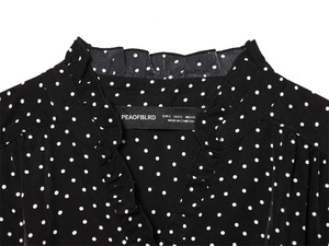 Detail view showing ruffled neckline and polka dot pattern with clothing brand neck label