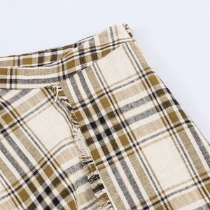 Macro detail of plaid mini skirt showing green checkered fabric texture and frayed hem
