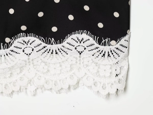 Detailed close-up of white floral lace trim stitched on black polka dot silky fabric