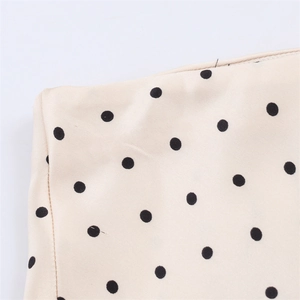Detail shot of the fine stitching and black polka dot pattern on beige woven fabric