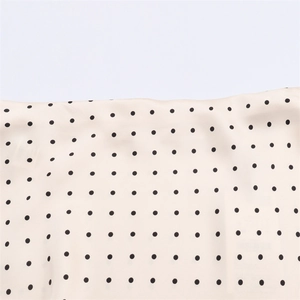 Close-up detail of soft cream fabric with classic black polka dots and fine stitching