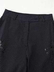 Detail of black pinstripe trousers featuring dragon sequin embroidery and button waist