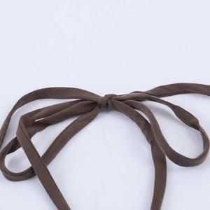 Dettaglio del fiocco in tessuto marrone scuro e del laccetto al collo dell'abito a pois
