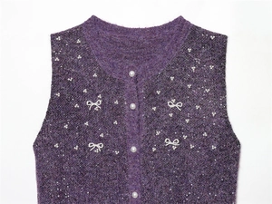 Detail of purple knit vest with white pearl bow pattern and shiny sequins close-up