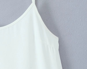 Detail of the white dress featuring a thin shoulder strap and fine seam stitching