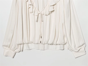 Detailed close-up of ivory silk shirt featuring ruffled V-neckline and delicate ties