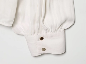 Close-up of white silk shirt cuffs featuring pleated details and dual metallic buttons