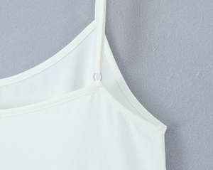 Detailed close-up of adjustable straps and metallic ring on white camisole top