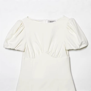 Robe blanche chic à manches bouffantes avec détails plissés et coupe ajustée sur fond gris