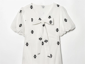 Close-up of white cotton dress featuring black floral embroidery and V-neck bow tie