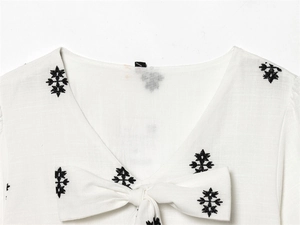 Detail of V-neckline with ethnic black embroidery and bow tie on white cotton fabric