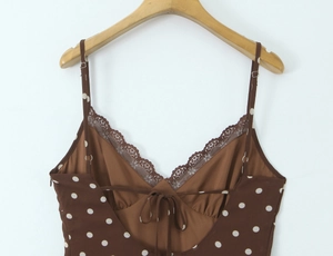 Détail du col en V avec dentelle florale brune et pois blancs sur un tissu marron