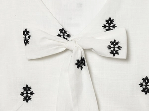 Detail of white cotton dress with bow tie neckline and black ethnic style embroidery