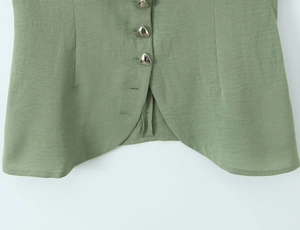 Detail of green vest featuring triangular metal buttons and stylish curved hemline