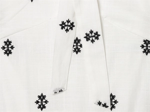 Detailed close-up of black geometric flower embroidery on white cotton dress fabric