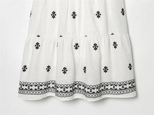 Detail of white cotton linen dress hem featuring black geometric embroidery and wavy edges