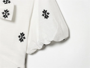 Detail of white cotton lantern sleeves with black cross-stitch floral embroidery patterns