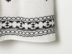 Detailed macro view of black floral embroidery on white cotton fabric dress hemline