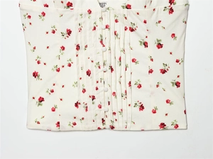 Close-up of white floral top featuring red rose prints, front buttons, and pleated details