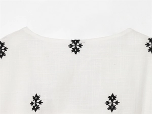 Detail of white cotton dress neckline with black geometric embroidery and texture