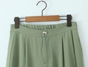 Detail view of light green trousers with triangle metal button and elastic waistband