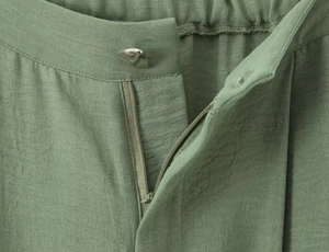 Detail of light green pants featuring silver button, zipper and elastic waistband texture