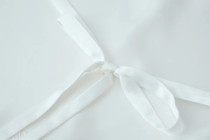 Close-up of white long sleeve top featuring a delicate lace splice and waist bow tie